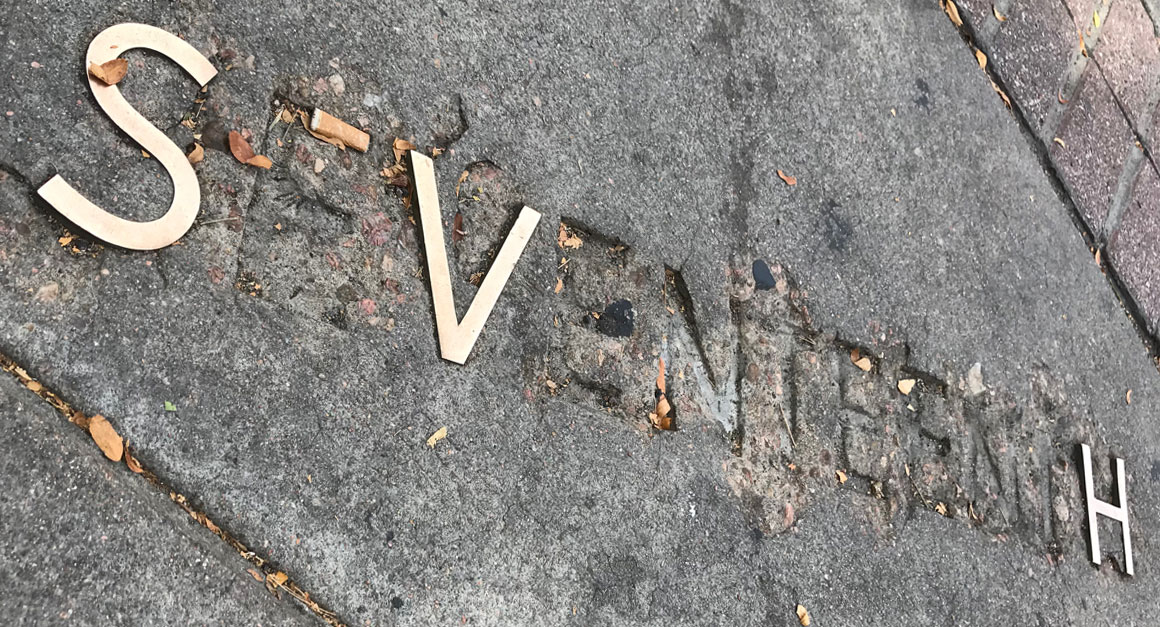 worn-out street name letters on a sidewalk